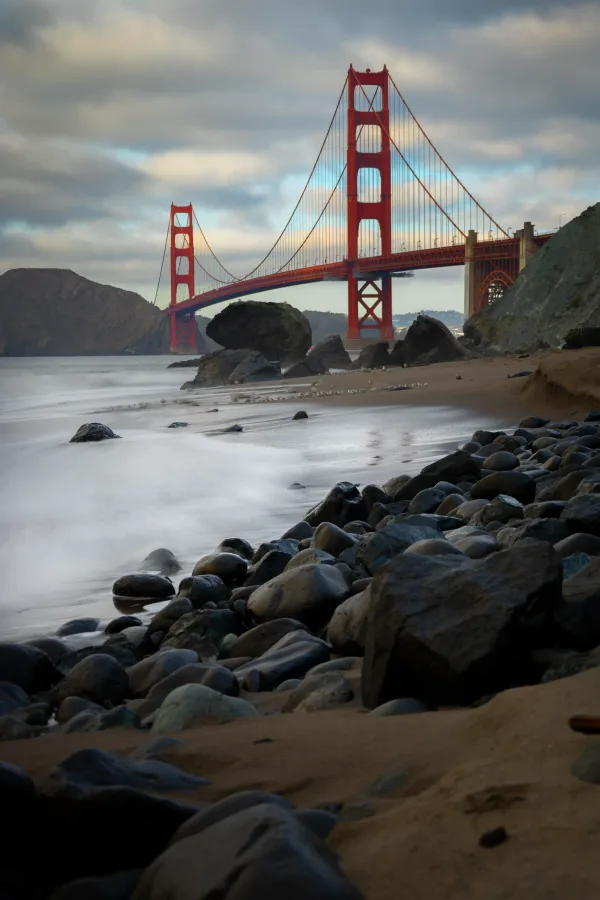 The Golden Gate Bridge above waves and rocks at Marshall’s Beach.