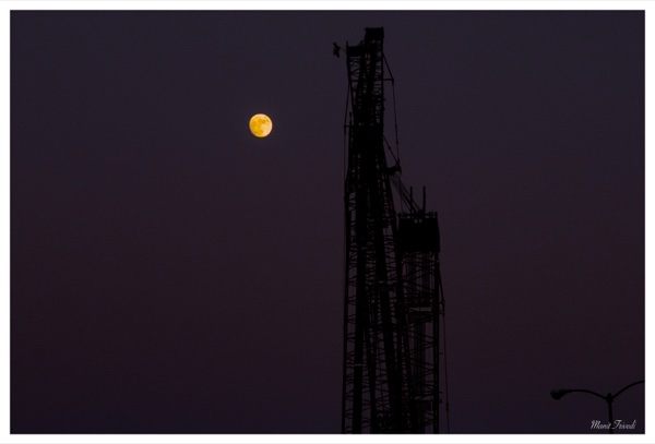 The moon hangs beside the silhouette of a construction tower.